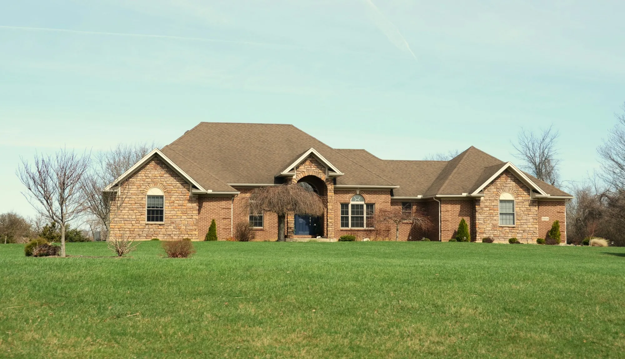 Brick ranch home with a brown shingle roof on a wide lawn