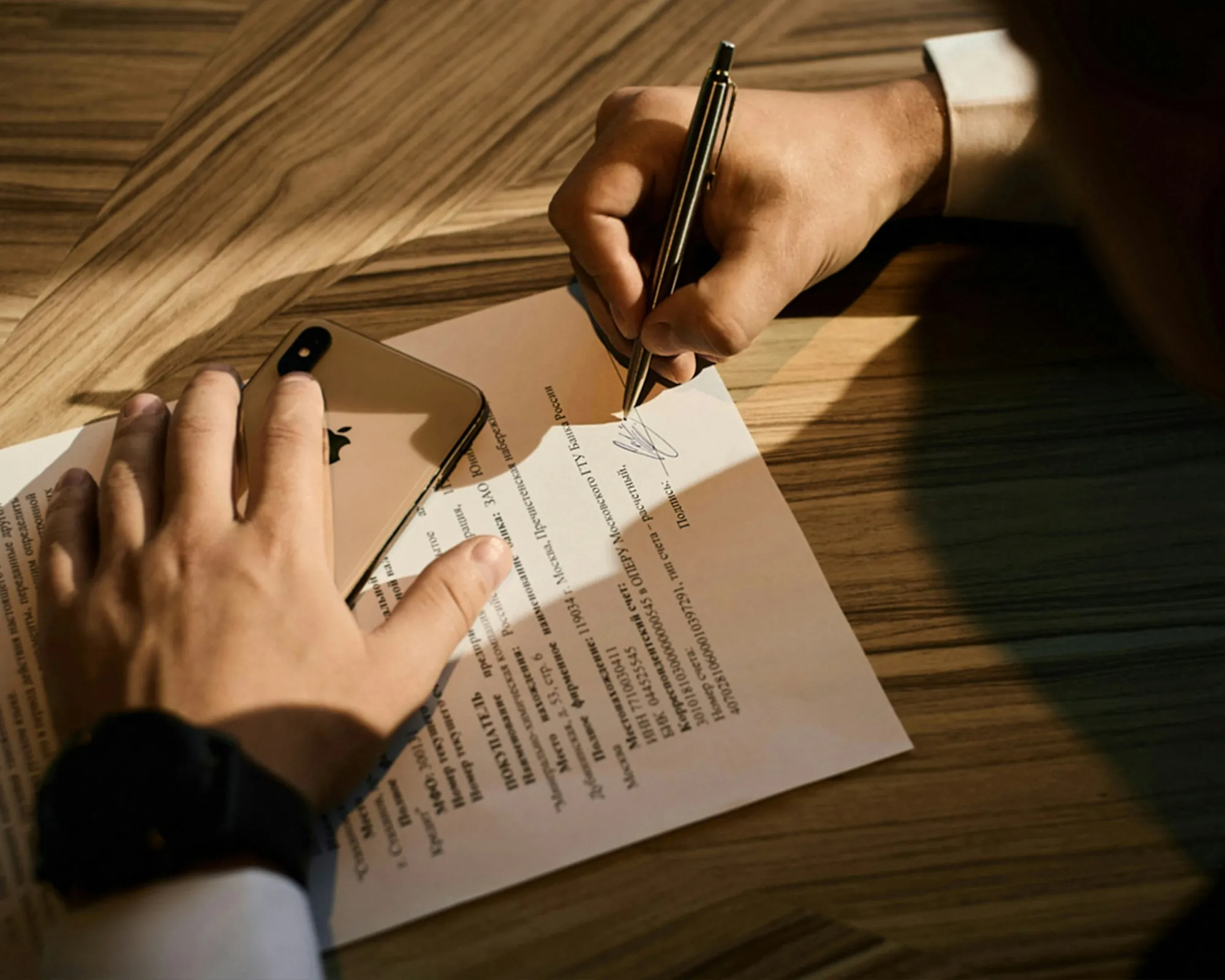 Hand signing a paper on a wooden table in warm light