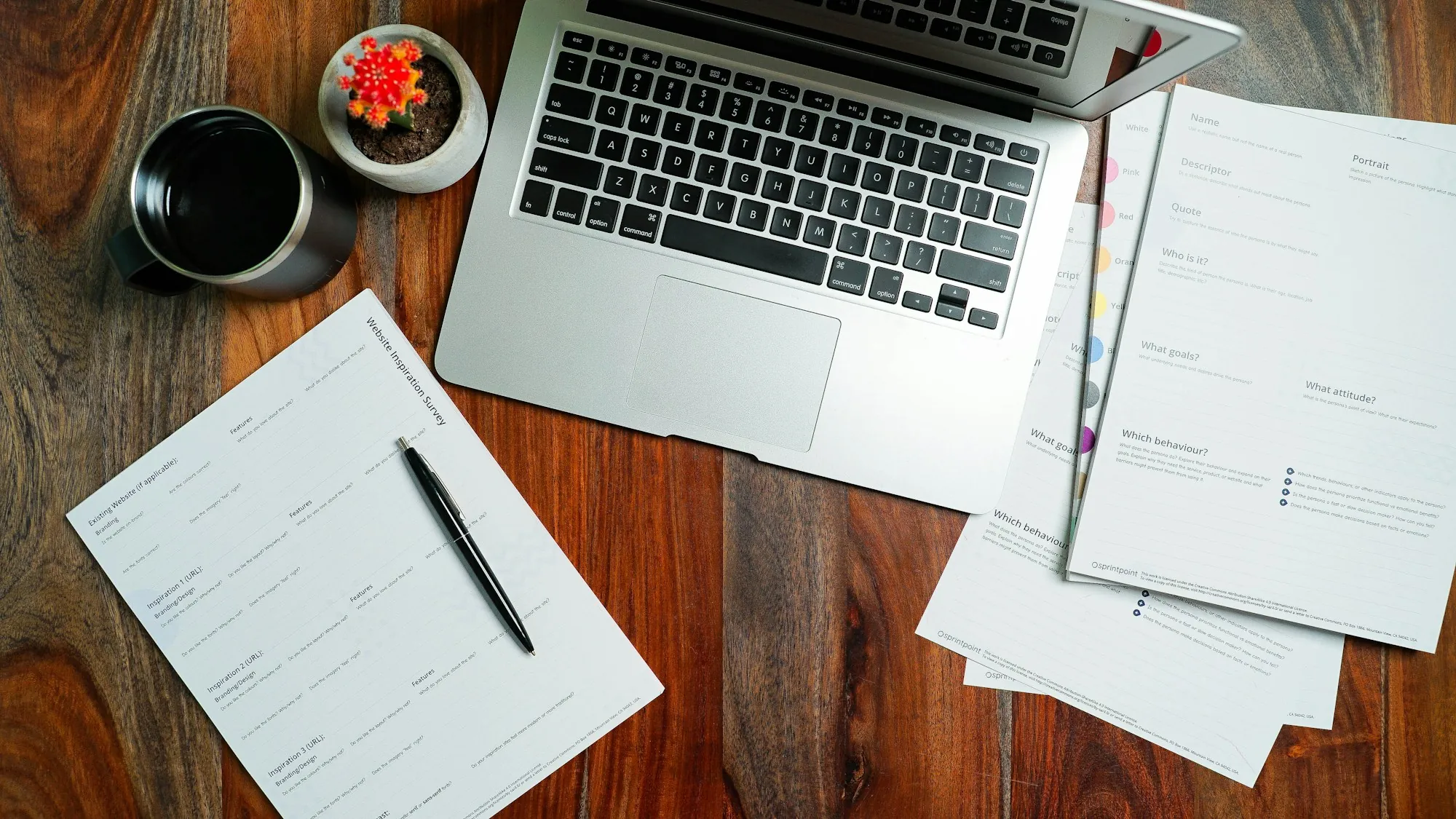 Forms, a pen and a laptop spread on a wooden desk