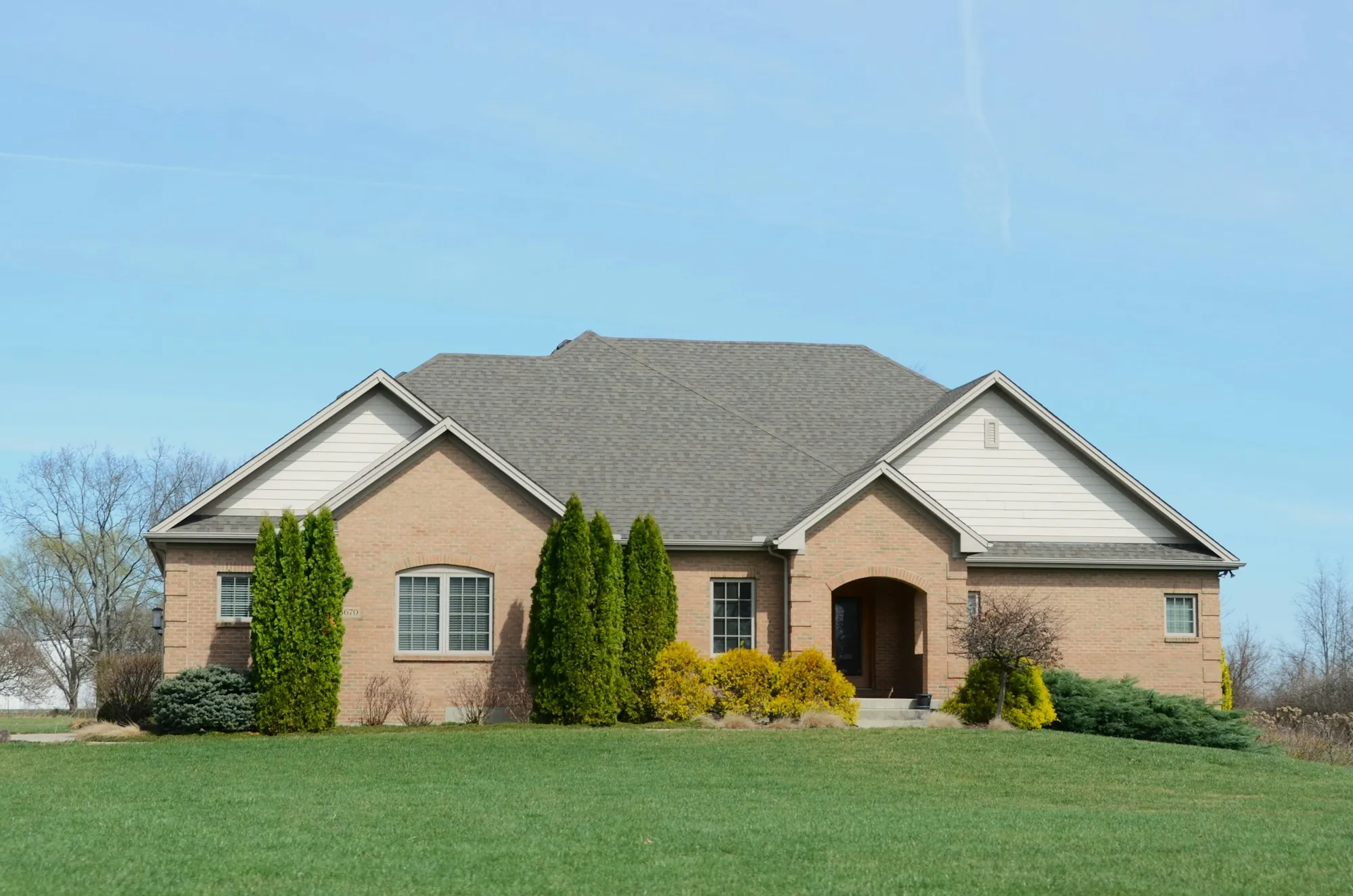 Brick ranch home with a hipped shingle roof and evergreen shrubs